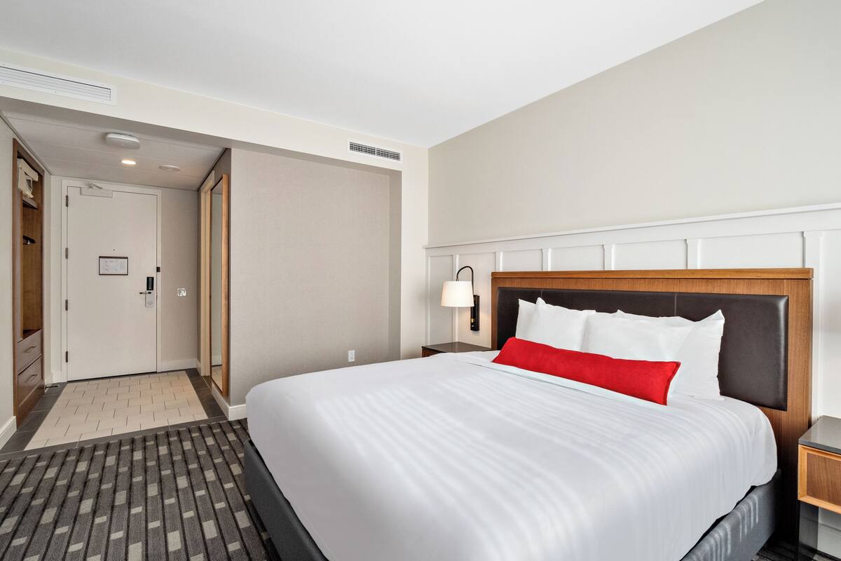 Une chambre d’hôtel avec un grand lit, une table de chevet avec une lampe, une tête de lit en bois et une porte donnant sur un placard.