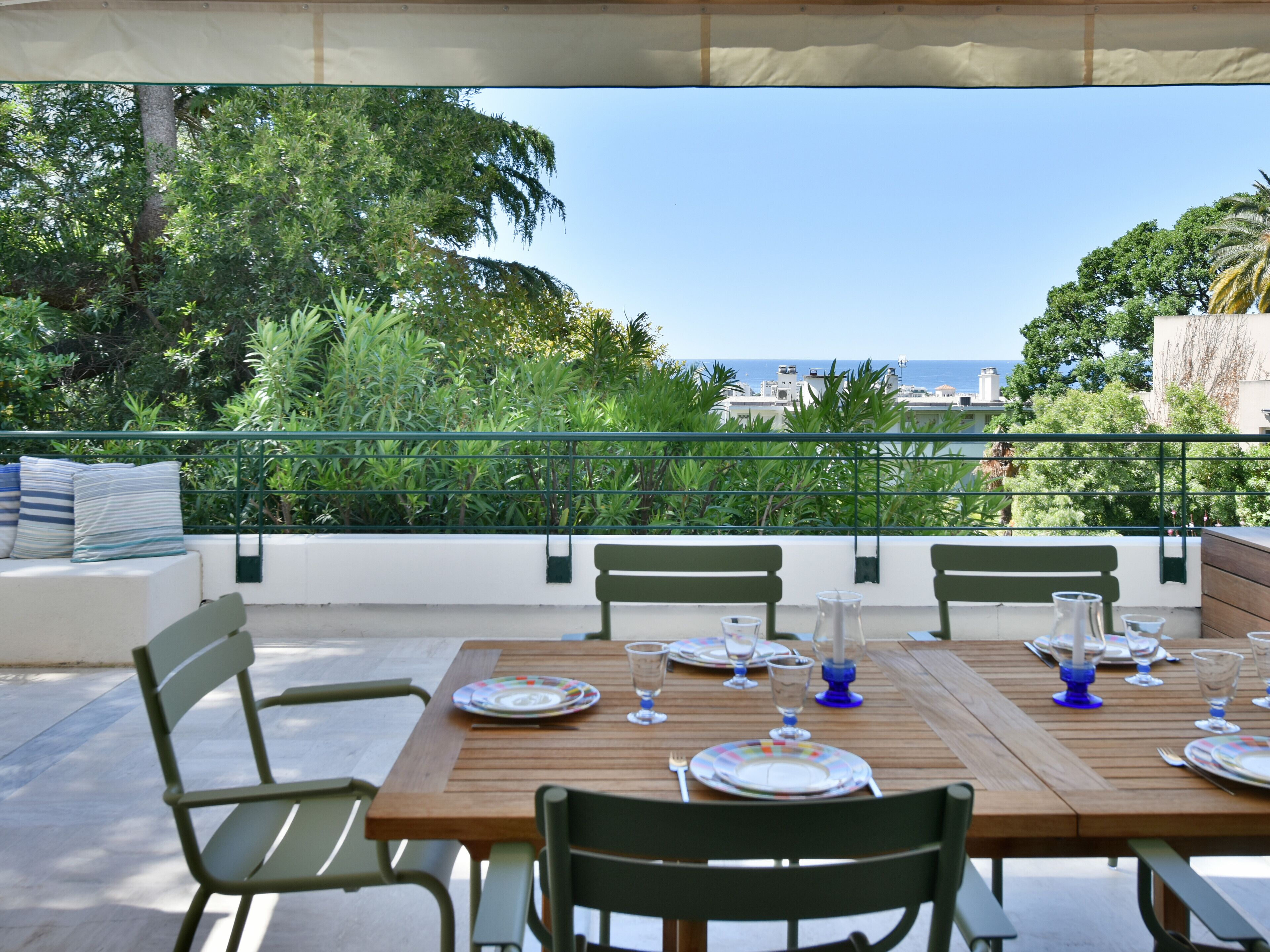 Un espace de restauration en plein air avec vue sur la mer, entouré de verdure et bordé d’un mur blanc.