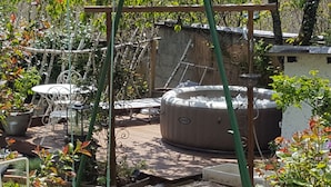 A hot tub in a garden with a wooden deck, surrounded by potted plants and a metal chair. - Les iris Chambres D Hôtes (Niedermorschwihr)