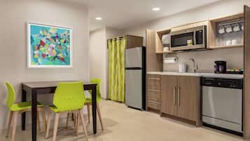 A modern kitchen with a microwave, refrigerator, and dishwasher. There is a dining table with chairs and a painting on the wall.