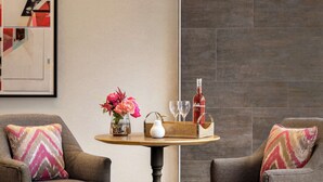 Una sala de estar moderna con dos sillones, una mesa redonda de madera, un jarrón con flores, una botella y dos vasos.
