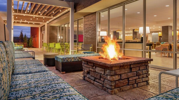 Un espacio al aire libre con zona de asientos con chimenea, asientos acolchados y un área de comedor con paredes de vidrio.