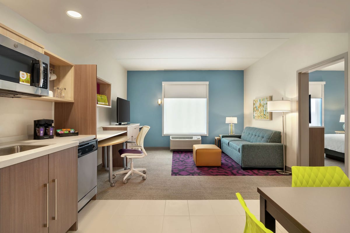 Una habitación de hotel compacta con kitchenette, escritorio, sofá y cama.