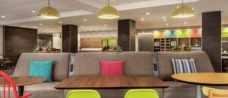 A modern interior with a seating area featuring a sofa and tables, overhead pendant lighting, and a kitchen area in the background.