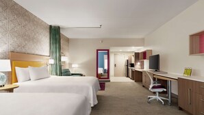 Habitación de hotel con dos camas, un escritorio, una silla, un televisor y un baño visible a través de una puerta.