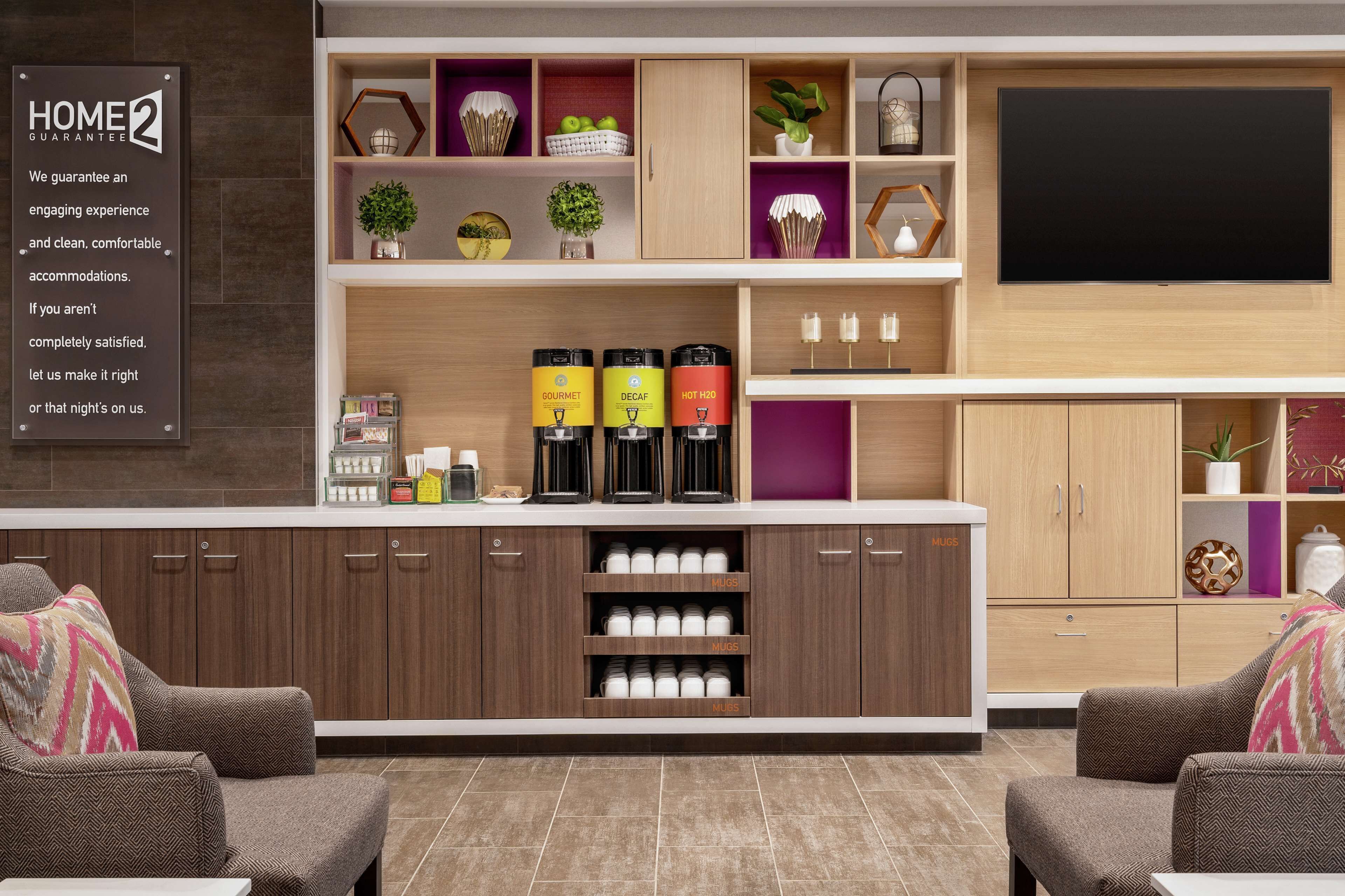 A modern living room with a coffee station, seating area, and a flat-screen TV mounted on the wall.