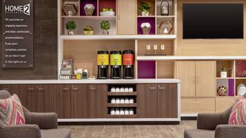 A modern living room with a coffee station, seating area, and a flat-screen TV mounted on the wall.