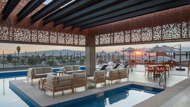 A rooftop pool area with lounge chairs, a pool, and a view of the sunset over the cityscape. - DoubleTree by Hilton Celaya (Celaya)