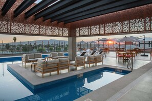 A rooftop pool area with lounge chairs, a pool, and a view of the sunset over the cityscape. - DoubleTree by Hilton Celaya (Celaya)