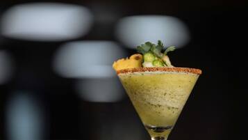 A cocktail in a martini glass with a salted rim, garnished with a slice of lime and a sprig of cilantro.