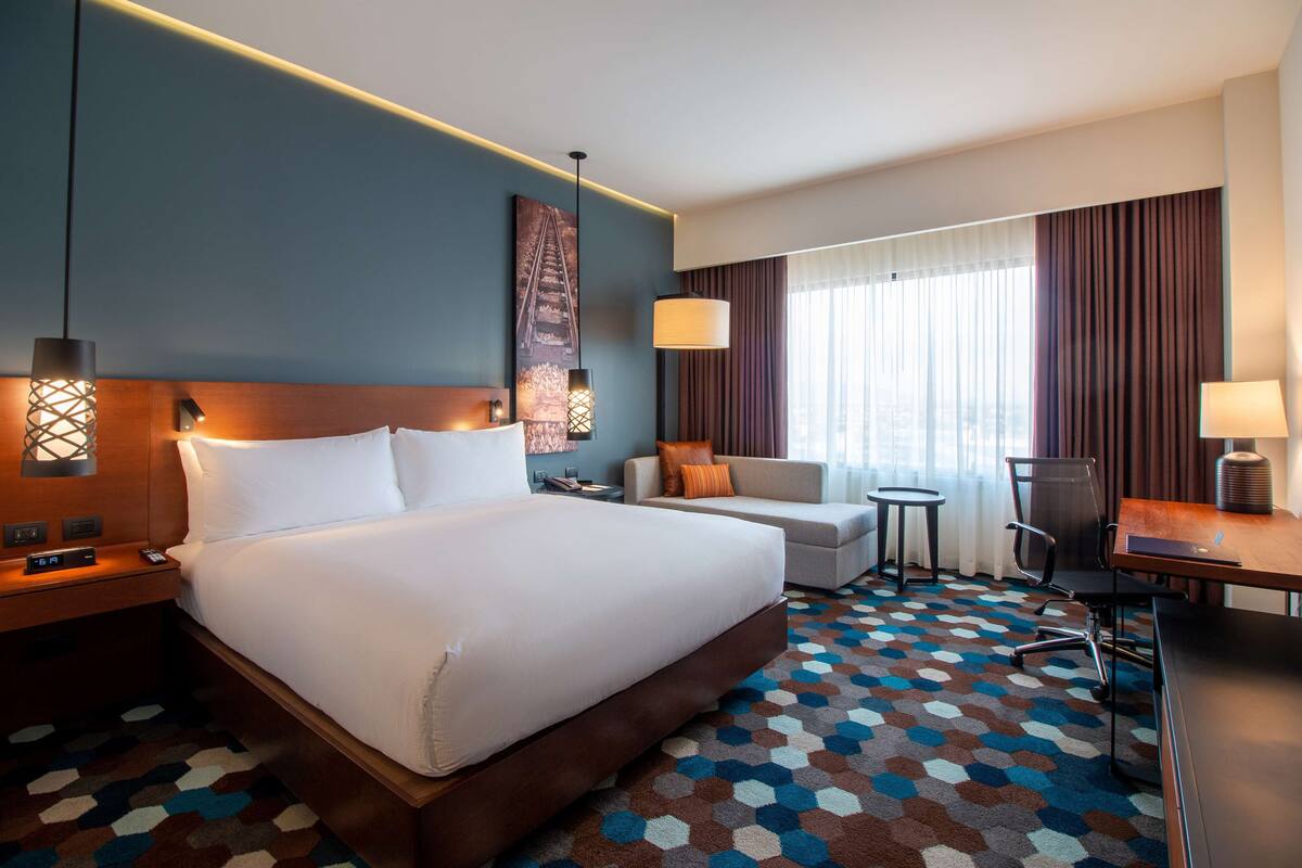 Quarto de hotel com uma cama grande, uma escrivaninha, uma cadeira, um sofá e uma mesa pequena.