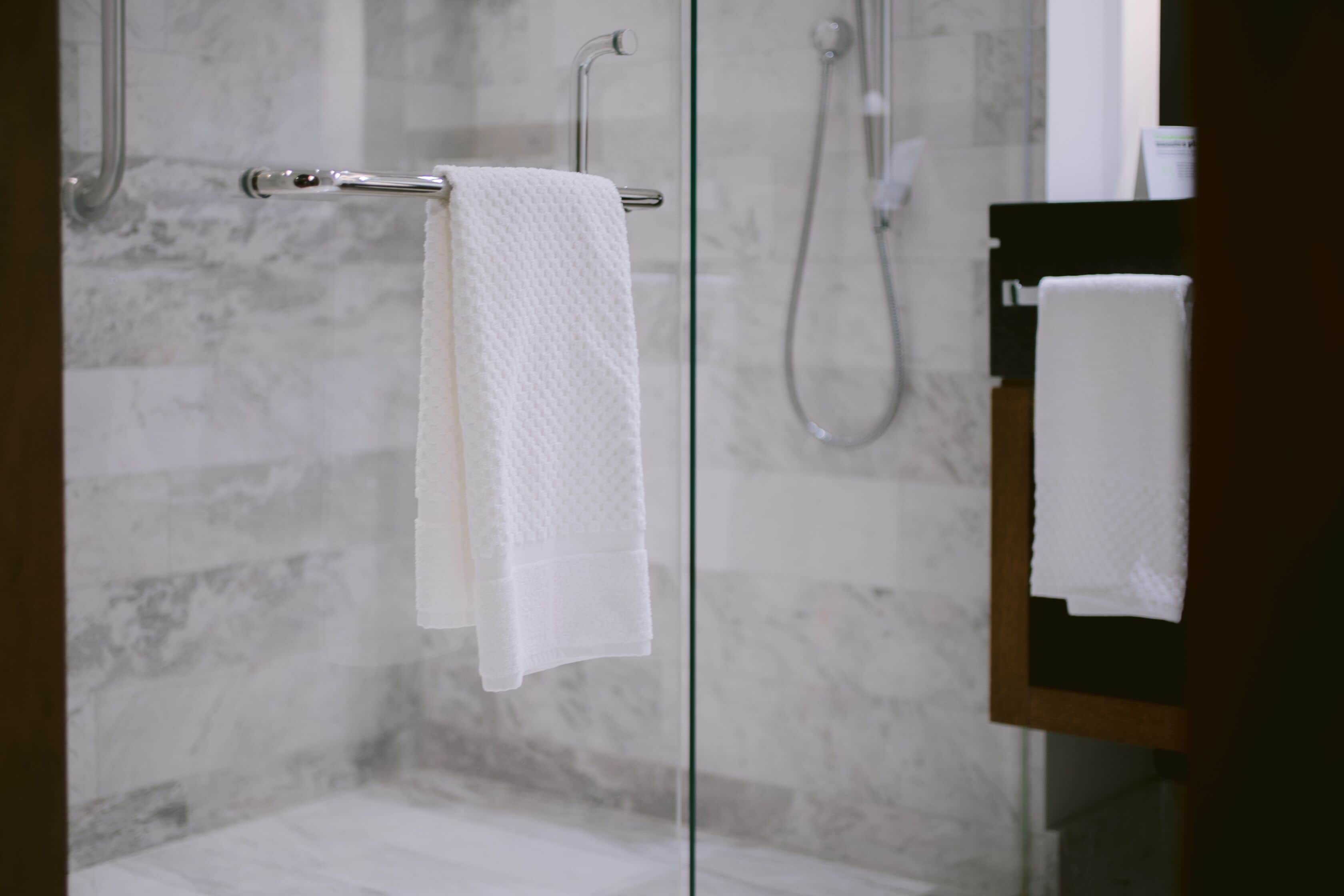 A glass-enclosed shower area with a towel rack holding two white towels.