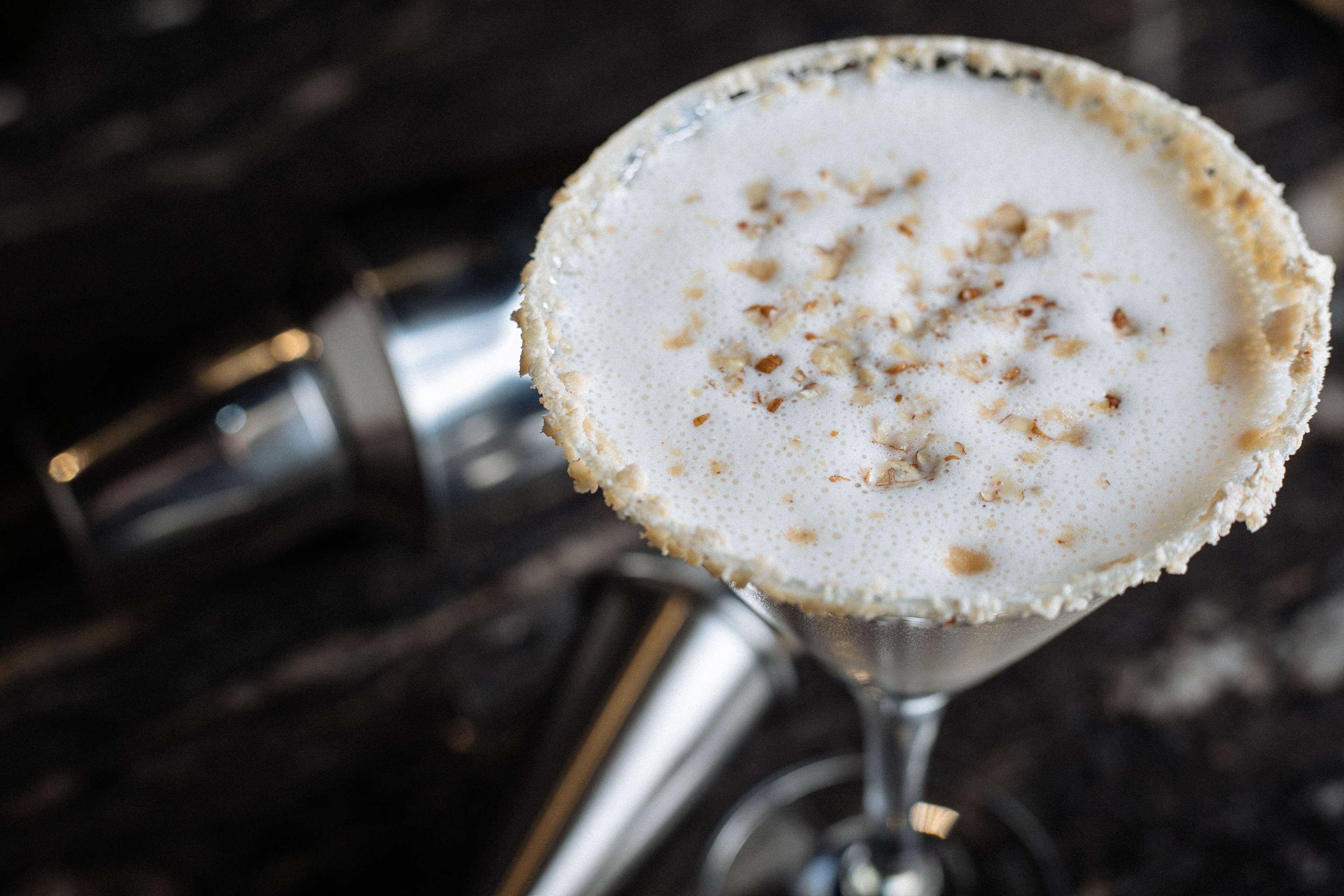 A cocktail in a martini glass with a frothy top and a rim sprinkled with spices.