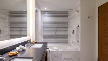 A modern bathroom with dual sinks, a large mirror, a shower with a glass door, and a wooden door.
