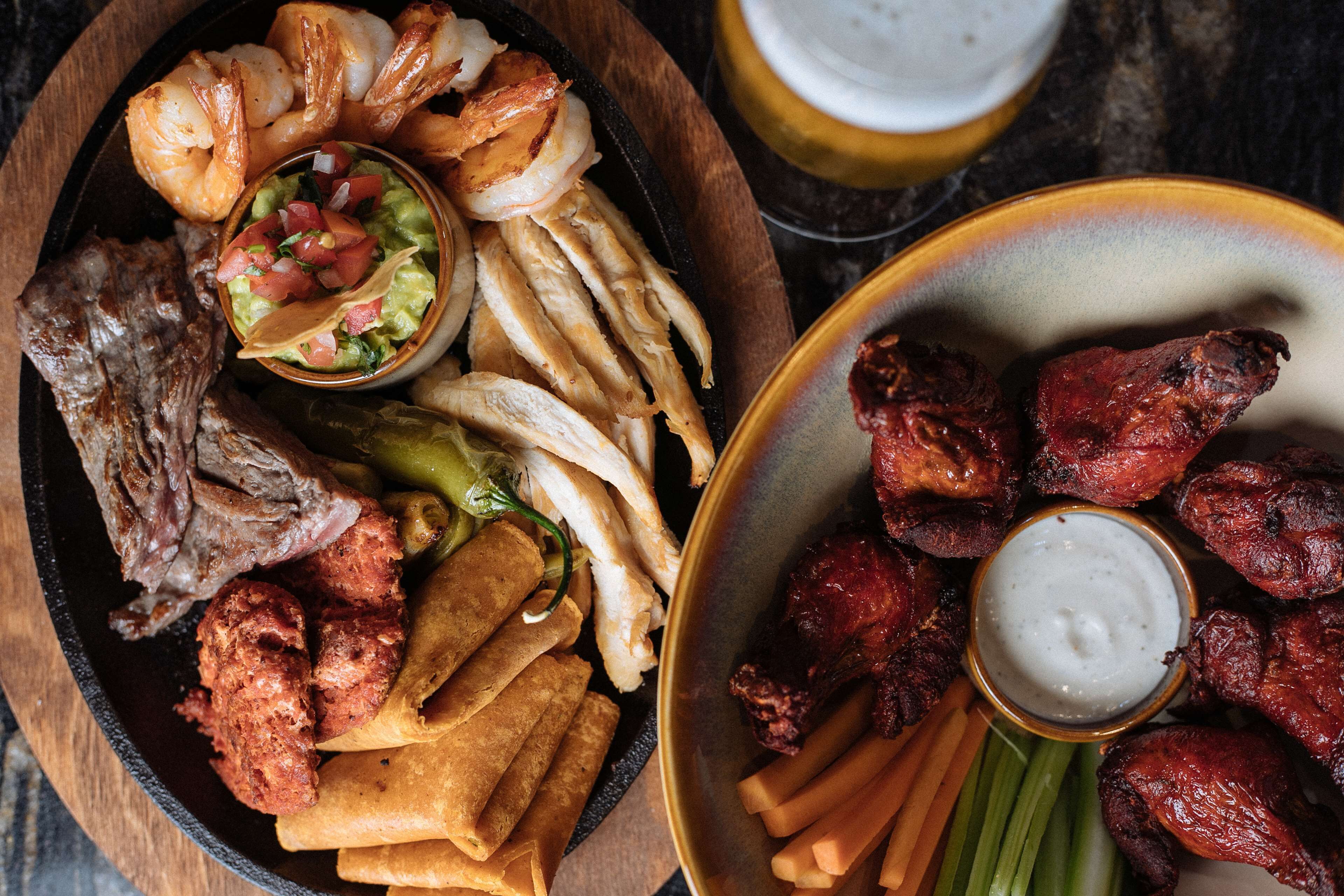 Diversas carnes a la parrilla y verduras, entre ellas camarones, pollo y costillas, servidas sobre una mesa de madera.