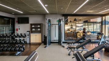 Un gimnasio con equipo de levantamiento de pesas, bancos y mancuernas.