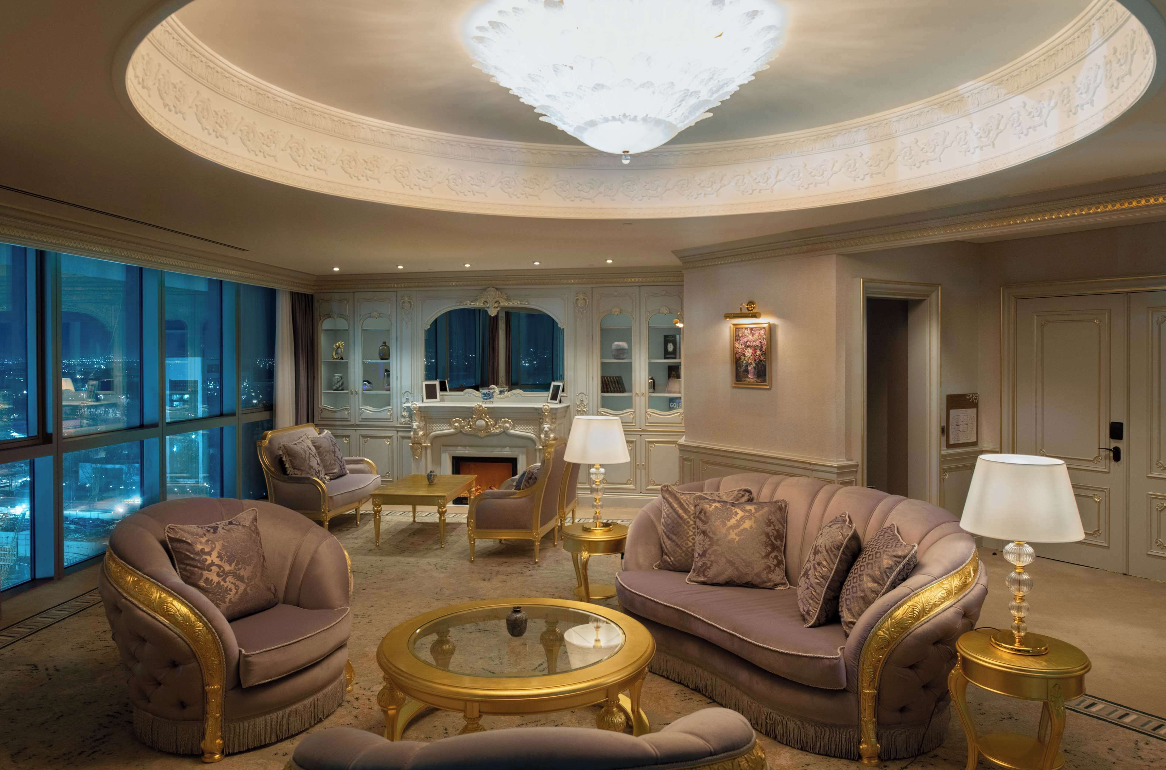 A luxurious living room with a fireplace, elegant furniture, and large windows offering a city view.