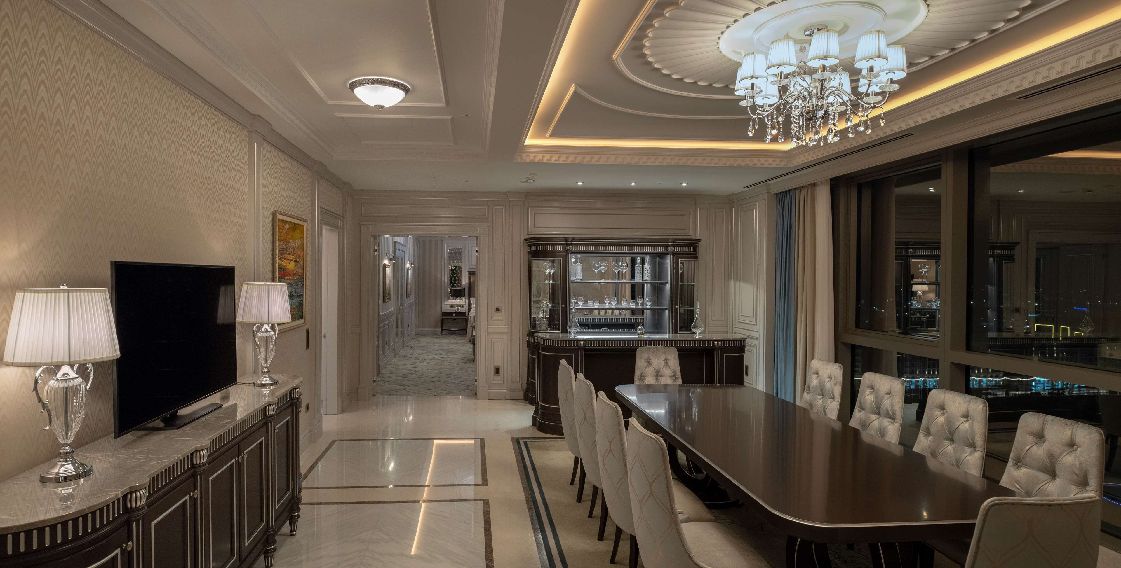 A spacious dining area with a long table and multiple chairs, a television, and a bar area with glassware.