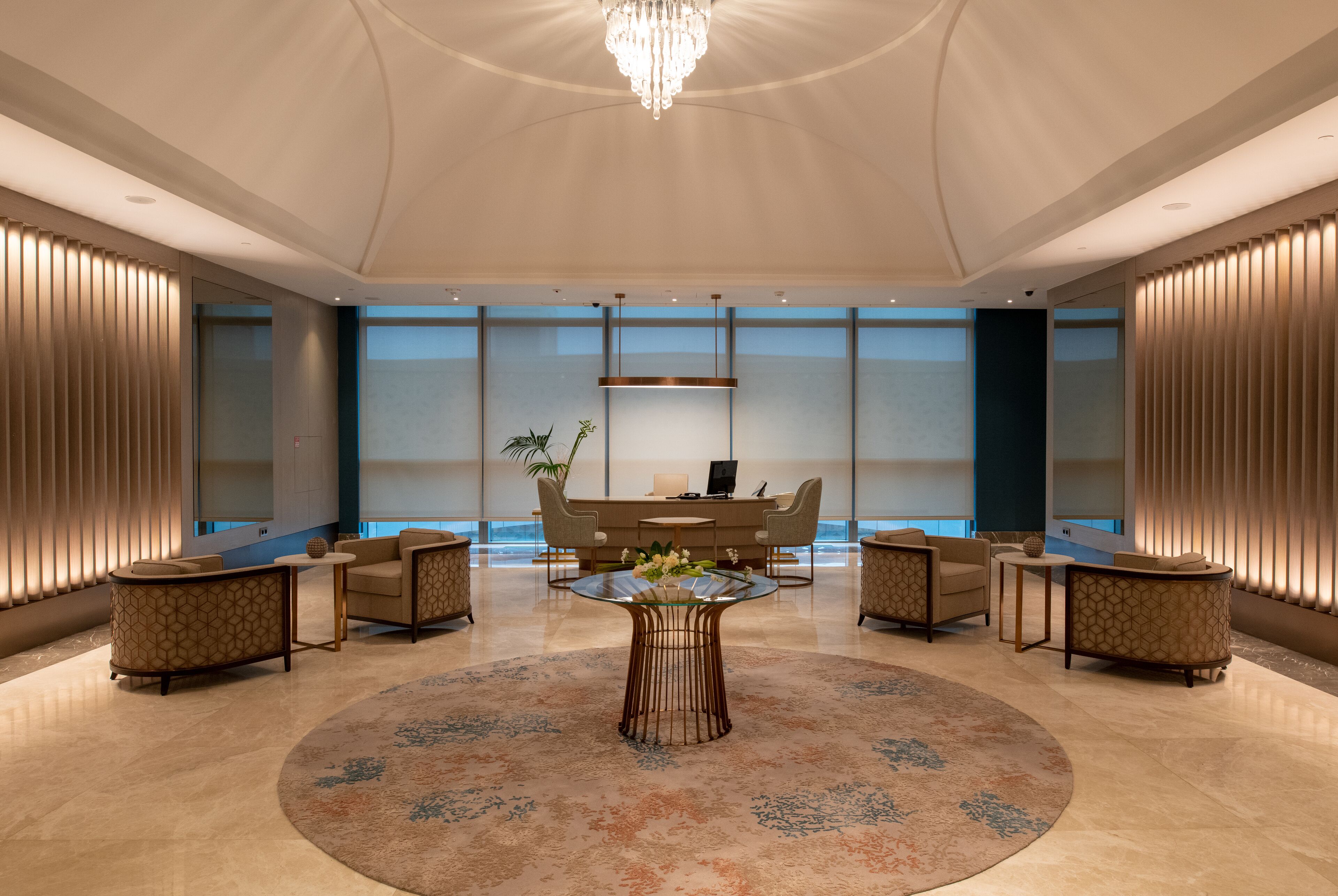 A spacious lobby with a central round table, seating arrangements, and a chandelier.