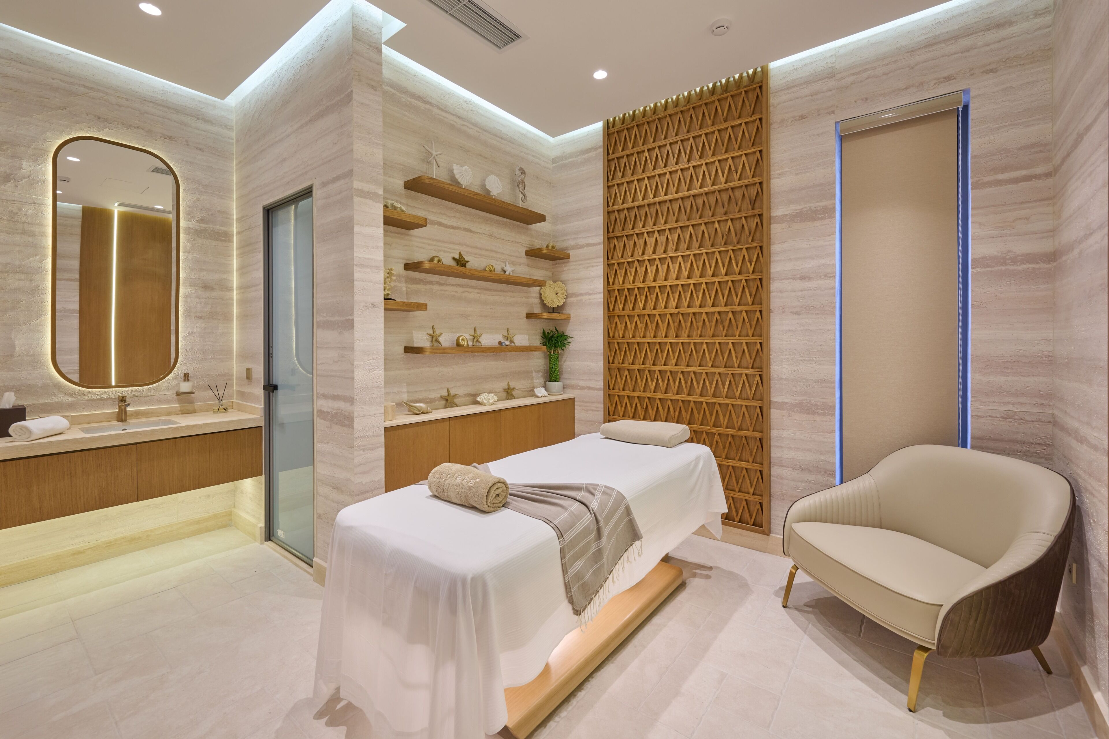 Un baño moderno con un espejo grande, un tocador con lavabo, una camilla de masaje y una silla.