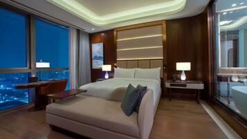 A modern hotel room with a large bed, a desk, and a view of the city at night.
