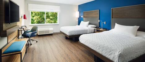 A hotel room with two beds, a TV, a desk, and a chair.