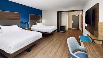 A hotel room with two beds, a desk, a chair, a TV, and a door leading to another room.