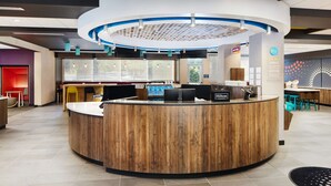 A modern reception area with a wooden reception desk, a circular blue and white ceiling design, and a seating area with yellow chairs. - Tru by Hilton Atlanta Northlake Parkway, GA (Atlanta)