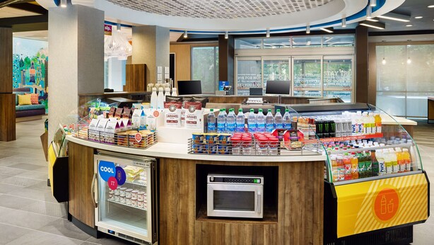 A self-service beverage station with a microwave, various drinks, and snacks. - Tru by Hilton Atlanta Northlake Parkway, GA (Atlanta)