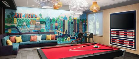 A pool table with a red felt surface, a sofa with colorful cushions, and a mural depicting Atlanta's skyline.