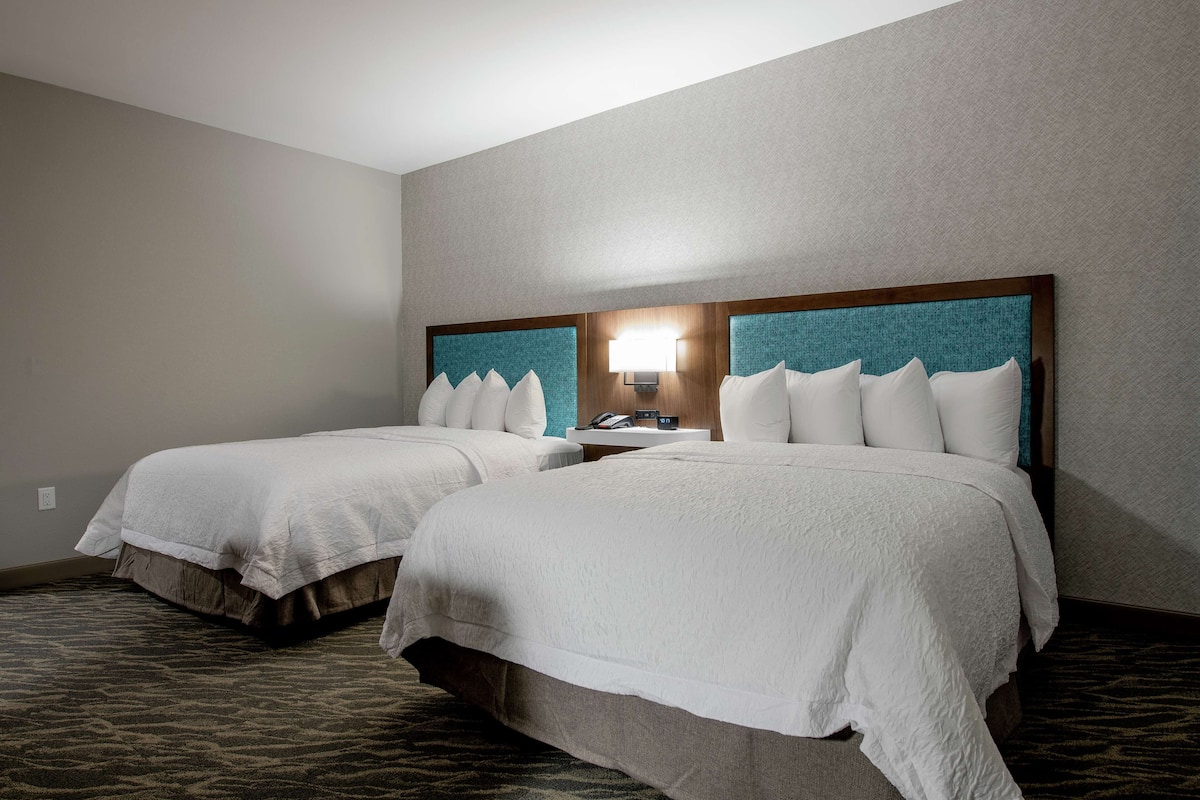 A hotel room with two beds, a nightstand with a lamp, and a patterned carpet.