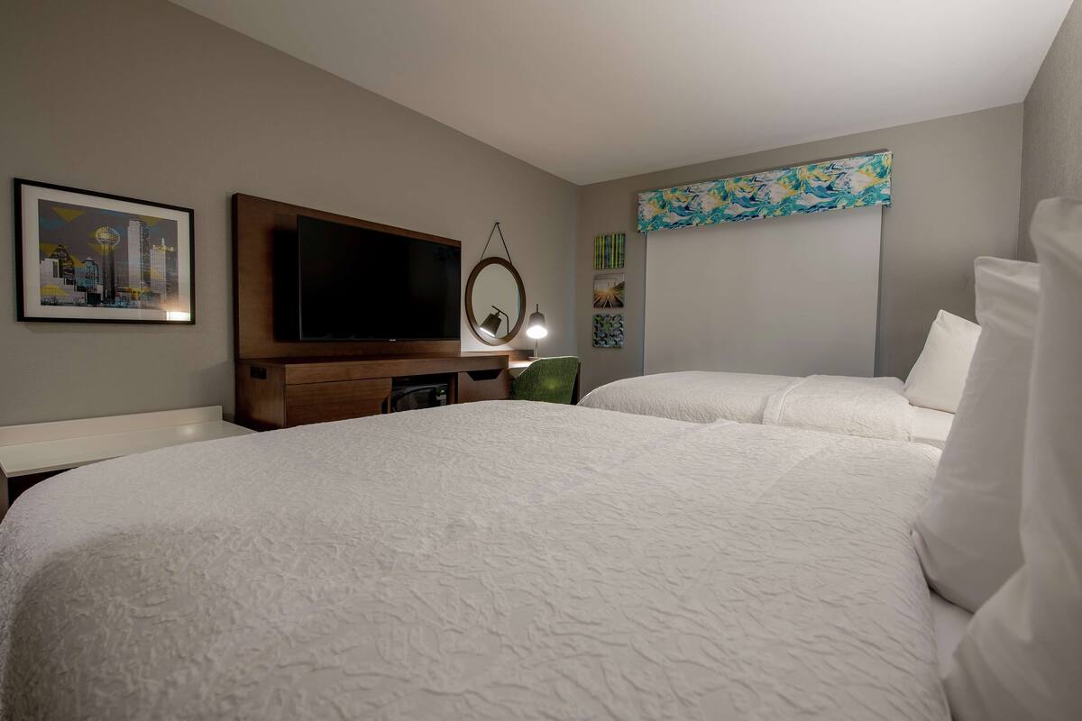 A hotel room with two beds, a flat-screen TV, a mirror, and artwork on the walls.