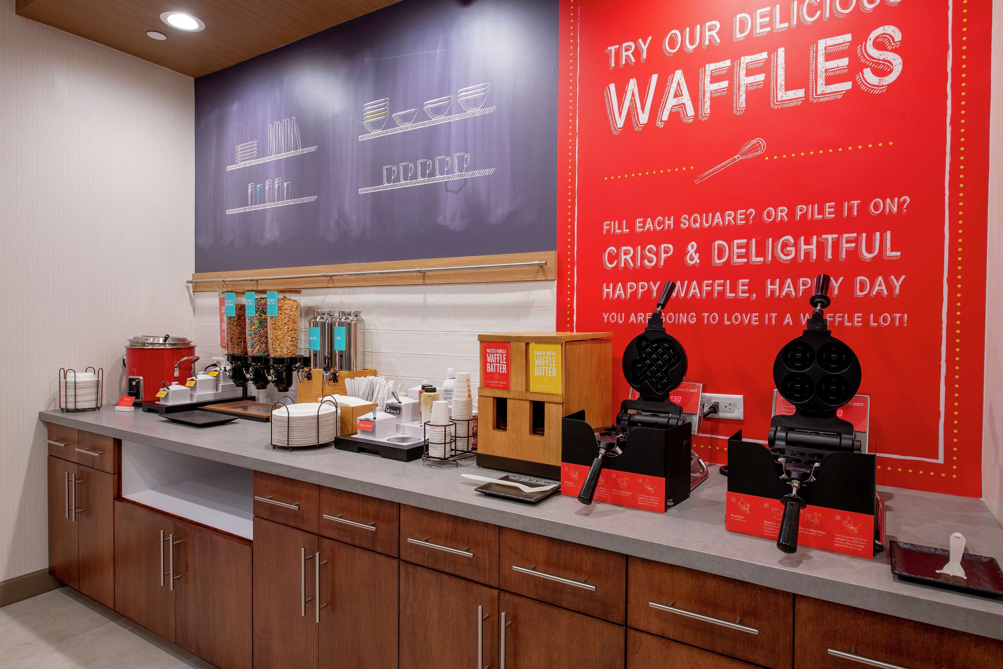 A kitchen counter with waffle-making equipment, waffle batter dispensers, and a waffle iron.
