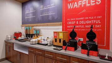 A kitchen counter with waffle-making equipment, waffle batter dispensers, and a waffle iron.