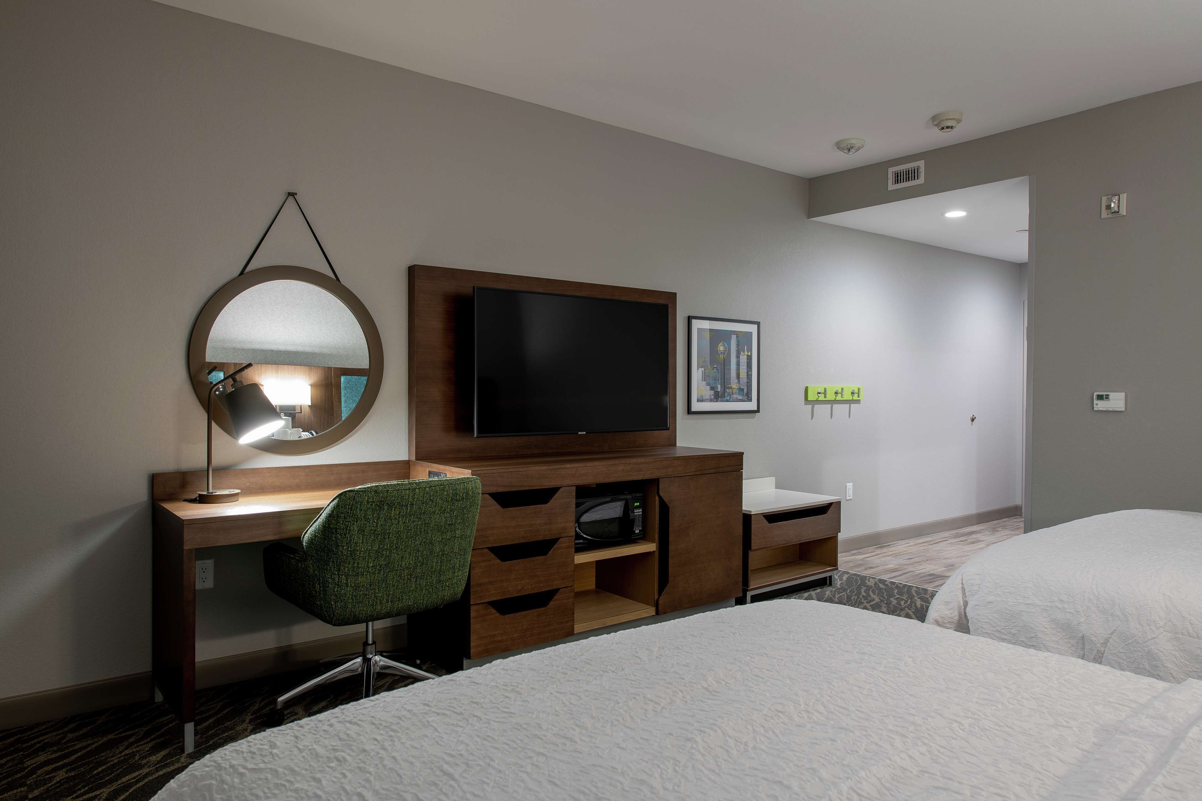 A hotel room with a bed, a desk with a chair, a television, and a mirror.