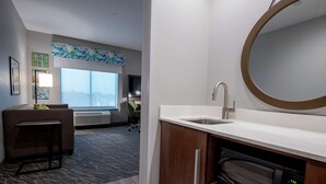 A hotel bathroom with a sink, mirror, and microwave. There is a bar stool and a large window in the background. - Hampton Inn & Suites Duncanville Dallas (Duncanville)