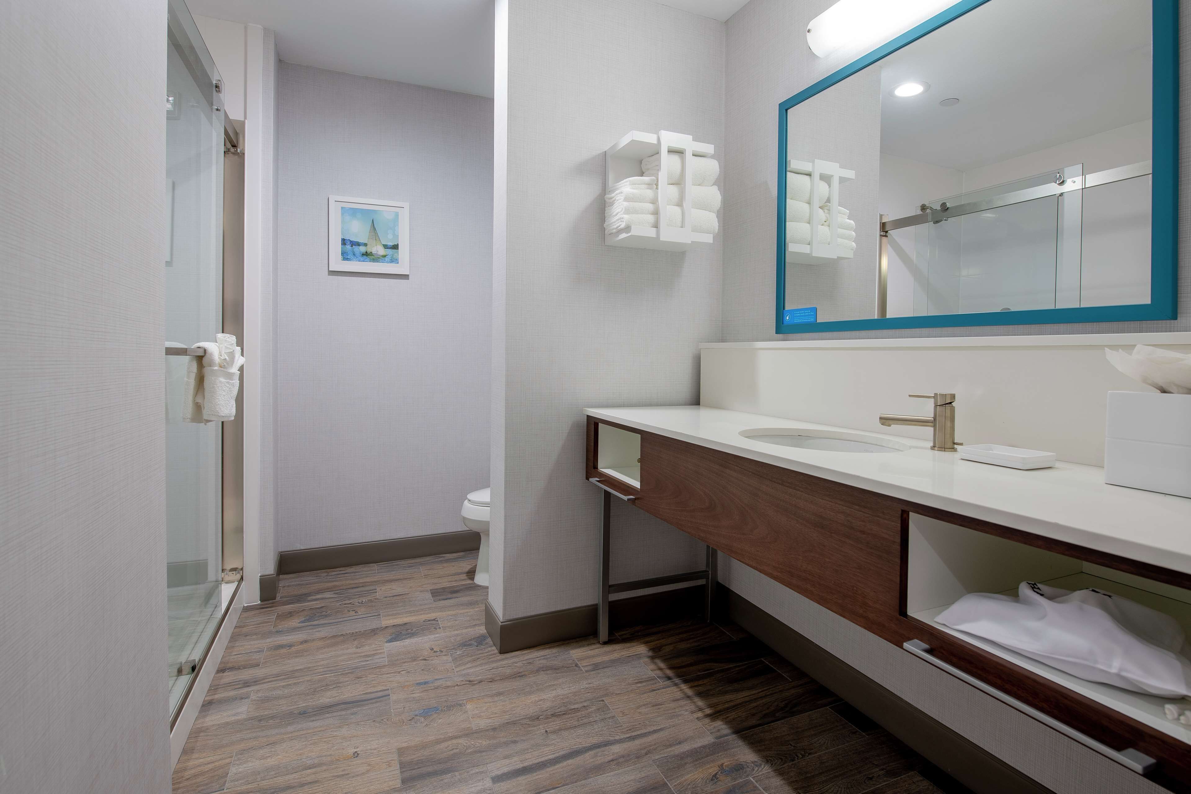 A modern bathroom with a glass shower enclosure, a wooden vanity, a large mirror, and a towel rack.