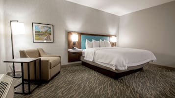 A hotel room with a bed, a desk, a chair, a nightstand, a lamp, and a framed picture on the wall.