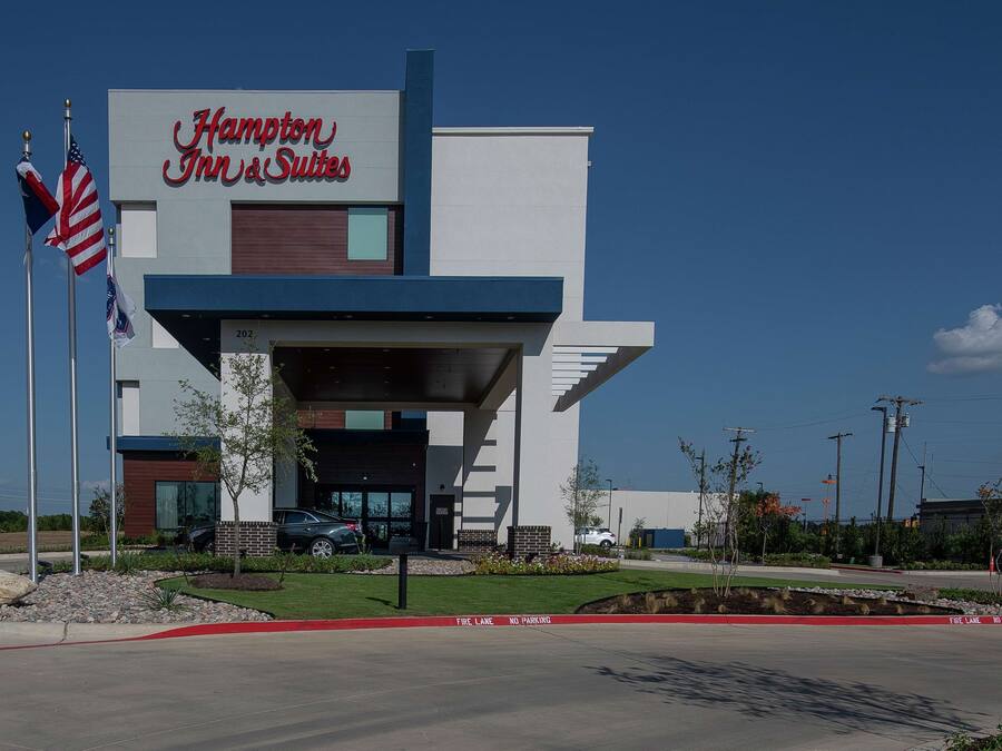 A Hampton Inn & Suites building with a modern design, a covered entrance, and an American flag.