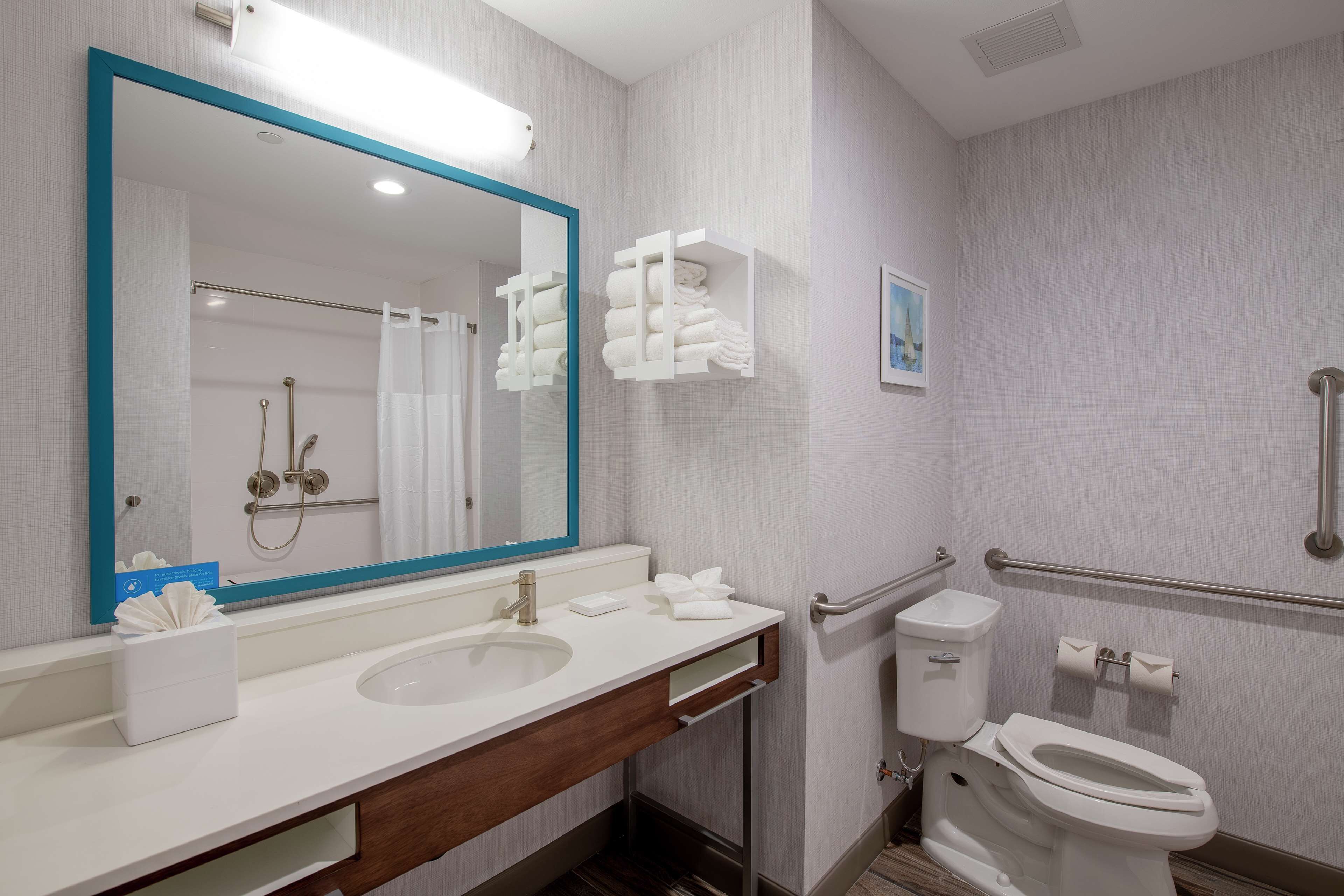 A modern bathroom with a large mirror, two sinks, a toilet, and a shower area.