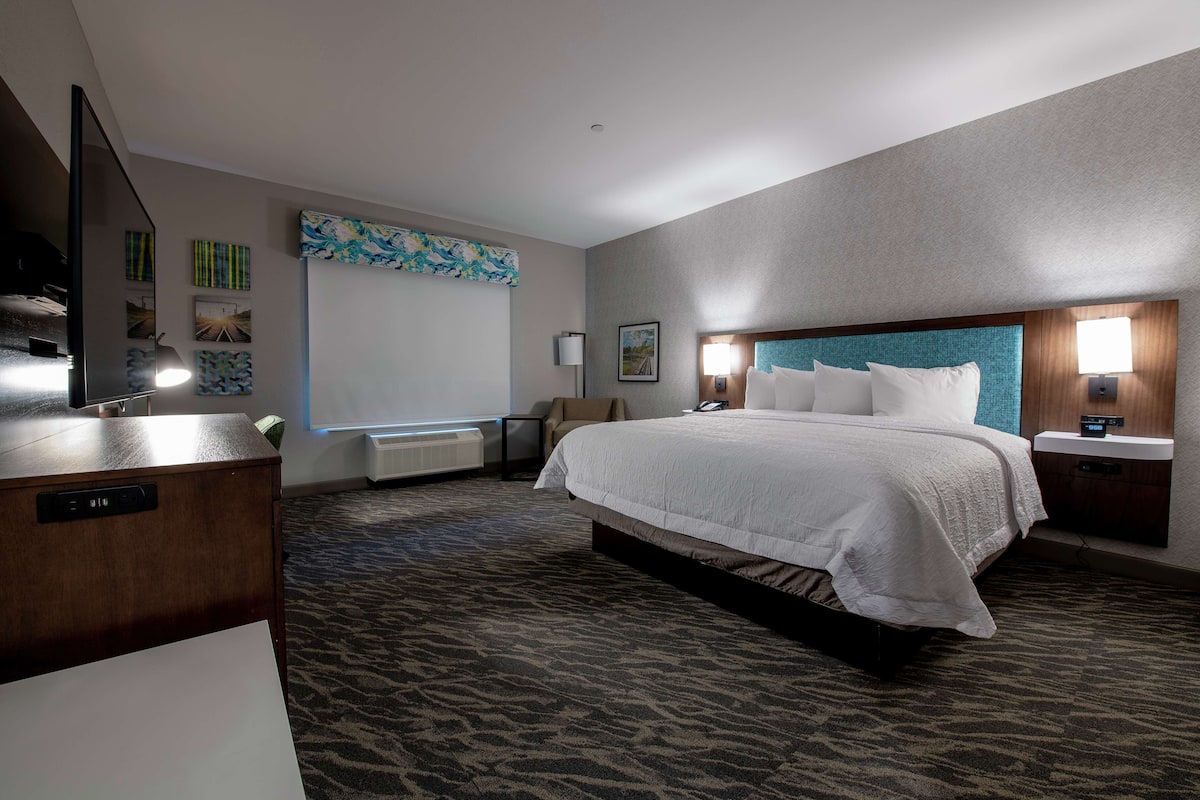 A hotel room with a large bed, a desk, a chair, and a TV.