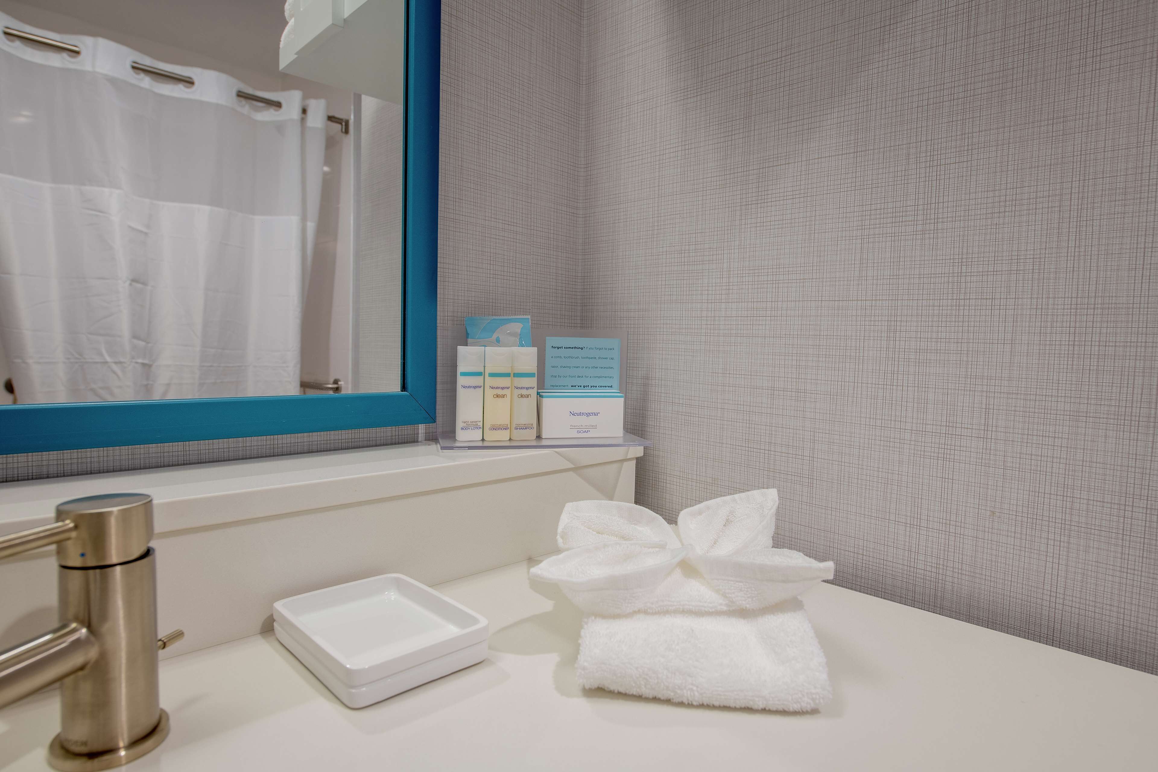 A bathroom with a white sink, a mirror, and a towel with a bow. There are toiletries on the counter.