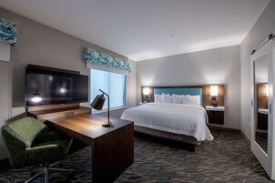 A hotel room with a bed, a desk with a chair, a television, and a window with a view.