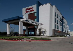 A Hampton Inn & Suites hotel with a modern design, featuring a covered entrance and a clear sky.