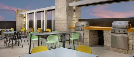 An outdoor patio with a stone wall, a grill, and a table with chairs.