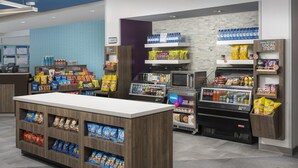 Un área de autoservicio con aperitivos y bebidas, que incluye diversas opciones de comida empaquetada, agua embotellada y un refrigerador.