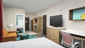 Habitación de hotel con cama, escritorio, silla, televisor, armario y una pequeña kitchenette.