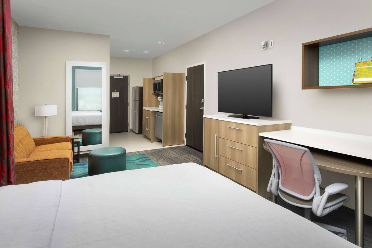 Una camera d'albergo con un letto, una scrivania, una sedia, una televisione, un armadio e un angolo cottura.