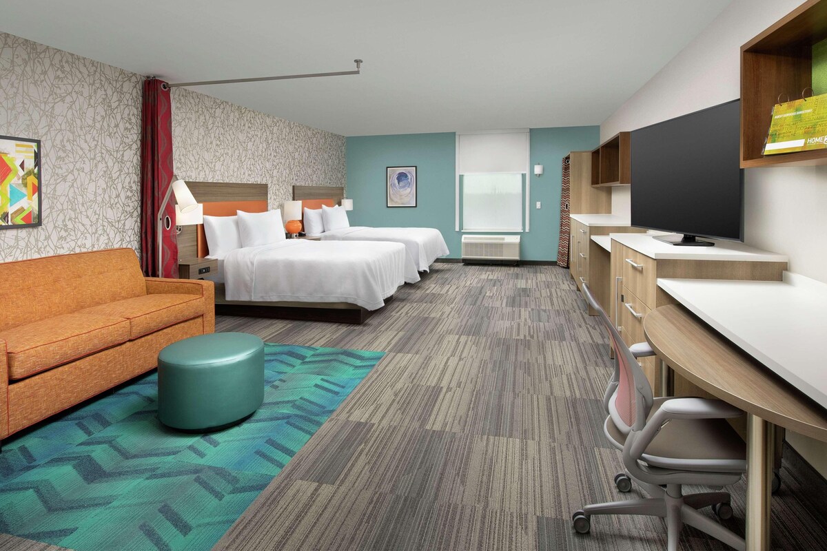 A hotel room with two beds, a sofa, a desk, and a television.