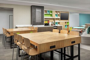 Eine moderne Hotelhalle mit einem Holztisch für Konferenzen, Stühlen, einer Rezeption und einer Kaffeestation.